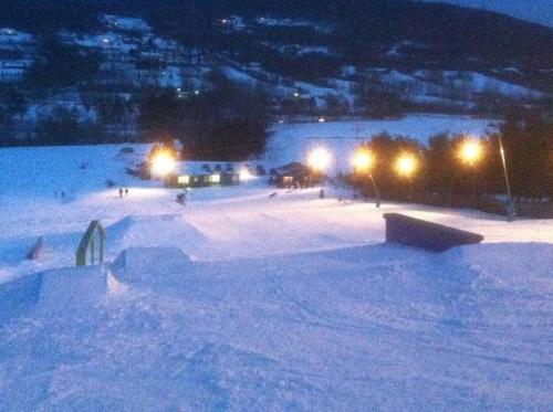 A snowy landscape at dusk with ski slopes, lights, and a small lodge in the background.