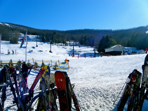 A snowy ski resort with ski equipment in the foreground, slopes and a clear blue sky in the background.