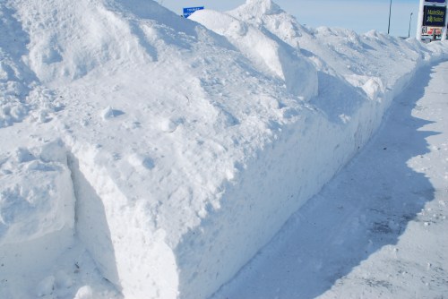 A large, snow-covered mound along a road, with a clear blue sky in the background.