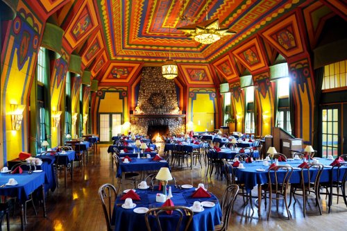 Colorful dining room with blue tablecloths, elegant decor, and a stone fireplace, featuring vibrant patterned walls and ceiling.