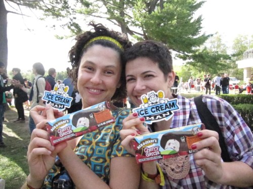 Two smiling women hold ice cream bars, each displaying "Ice Cream Man" stickers, in a sunny outdoor setting.