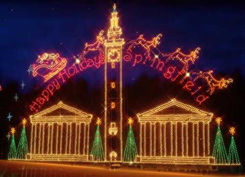 Colorful holiday lights display featuring a tower, buildings, and trees, with "Happy Holidays Springfield" in bright letters.