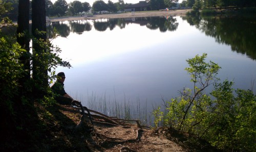 A serene lake surrounded by trees, with a person sitting by the water's edge, reflecting the calm scenery.