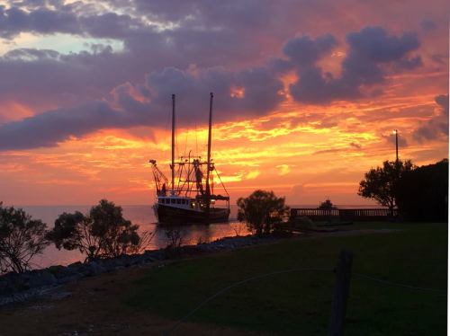 A fishing boat anchored near the shore at sunset, with vibrant orange and purple clouds reflecting on the water.