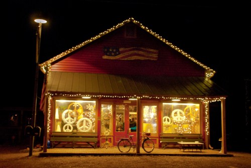 A cozy shop at night, adorned with string lights and a peace sign display, featuring a bicycle outside.