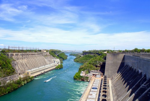 A scenic view of a river flowing between cliffs, with a bridge in the background and a dam on the right.