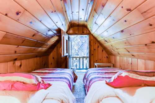 Cozy attic bedroom with two beds, wooden walls, and a window opening to a scenic view.