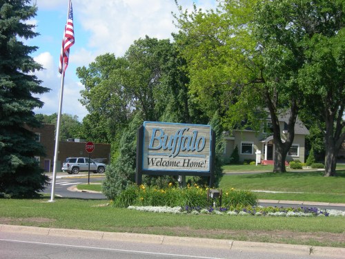 Welcome sign for Buffalo, surrounded by greenery and flowers, with an American flag in the background.