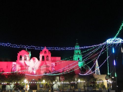 Colorful holiday lights illuminate a historic building at night, with festive decorations and a tree in the background.