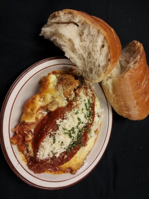 A plate of baked pasta topped with marinara sauce and cheese, served with a piece of crusty bread on the side.