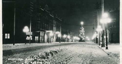 Historic black-and-white photo of a snowy street with a Christmas tree and illuminated buildings in Moscow, Idaho.