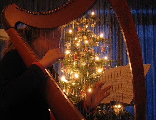 A person plays a harp in front of a decorated Christmas tree with twinkling lights.