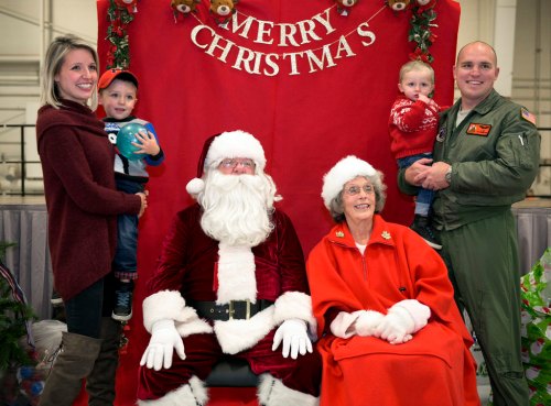 A family poses with Santa Claus and a woman in red, celebrating Christmas in a festive setting.