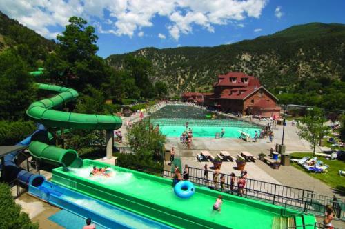 A water park scene featuring slides, pools, and people enjoying the outdoors with mountains in the background.