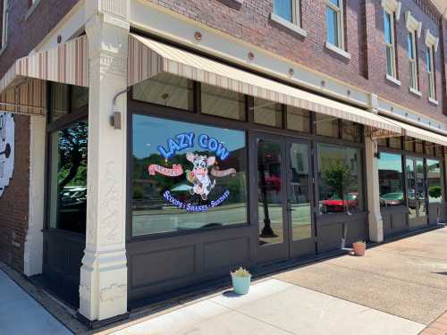 Exterior of the Lazy Cow ice cream shop, featuring a colorful sign and large windows with a striped awning.