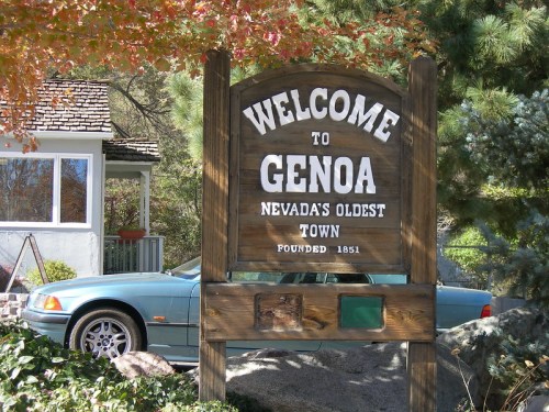 Welcome sign for Genoa, Nevada's oldest town, founded in 1851, with a car and greenery in the background.