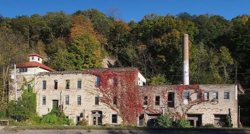 Abandoned stone building covered in ivy, with a tall chimney, surrounded by colorful autumn trees.