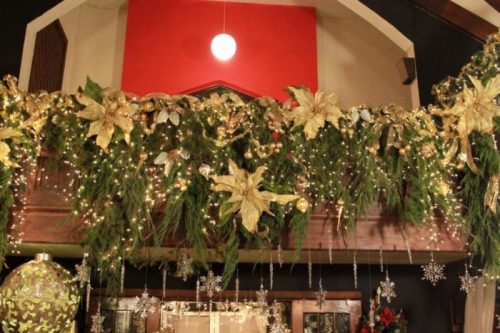 A festive garland adorned with gold flowers, greenery, and twinkling lights, hanging above a decorated space.
