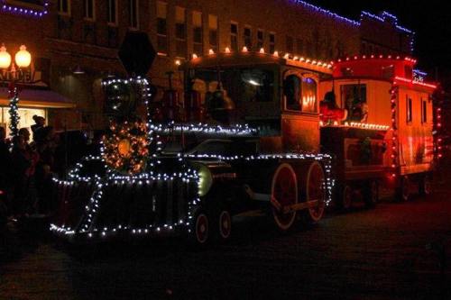 A brightly lit train decorated with holiday lights, moving through a festive night scene.