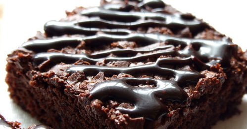 A close-up of a rich chocolate brownie drizzled with glossy chocolate sauce.
