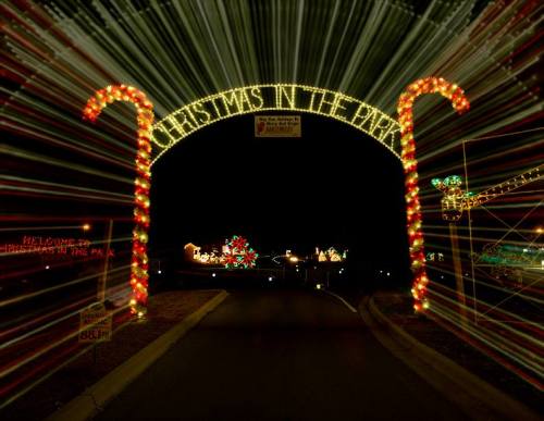 Colorful holiday lights form an archway reading "Christmas in the Park," illuminating a festive nighttime scene.