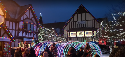 A festive market scene with colorful lights, decorated trees, and people enjoying the winter atmosphere at dusk.
