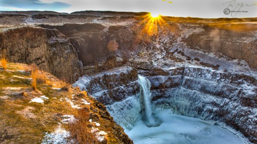 A stunning waterfall cascades into a frozen pool, surrounded by rugged cliffs and illuminated by a golden sunrise.