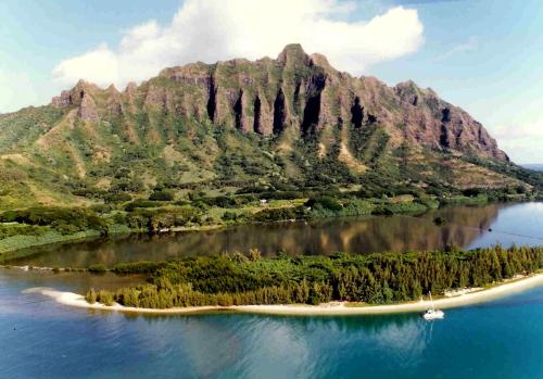 Aerial view of a lush green mountain with steep cliffs, surrounded by a river and a sandy beach.