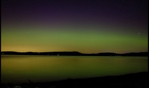 A serene night scene of a lake reflecting green and purple auroras under a starry sky.