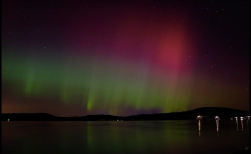 A vibrant display of the northern lights over a calm lake, with green and pink hues illuminating the night sky.
