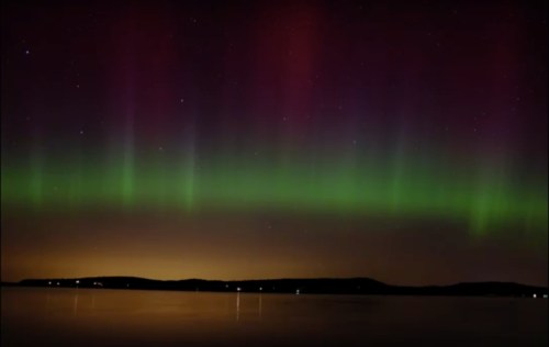 A stunning display of the northern lights with vibrant green and purple hues over a calm lake at night.
