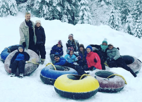 A group of people sitting on snow-covered ground with colorful snow tubes, surrounded by snowy trees.