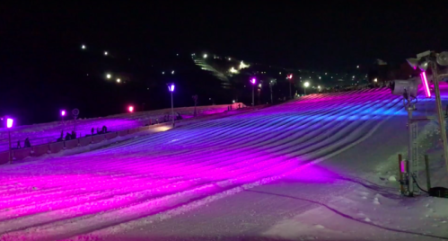 A snowy slope illuminated by colorful lights at night, with people enjoying the winter scenery.
