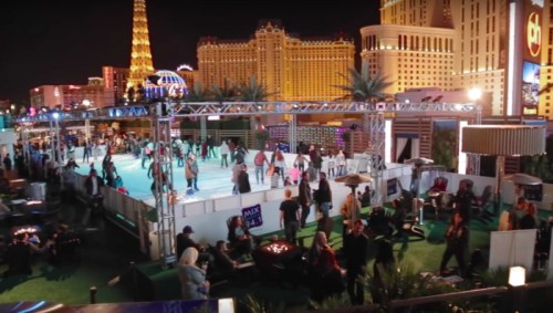 A bustling outdoor ice skating rink in Las Vegas, surrounded by bright lights and iconic buildings at night.