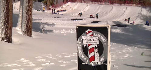 A snowy landscape with people sledding, featuring a sign for North Pole Tubing Park in California.