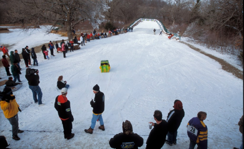 A snowy hill with spectators watching a sledding event, featuring a colorful sled racing down the slope.