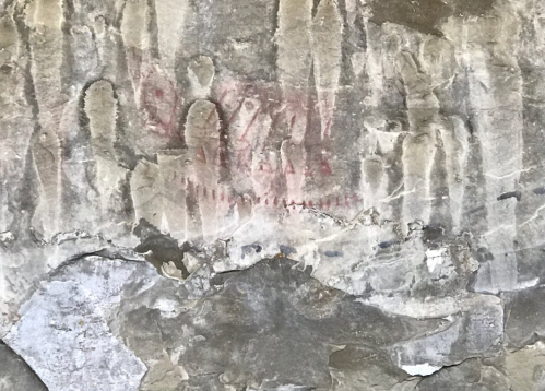 Ancient rock art featuring faded figures and symbols on a textured stone surface.