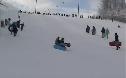 A snowy hill filled with people sledding and tubing, enjoying a winter day outdoors.