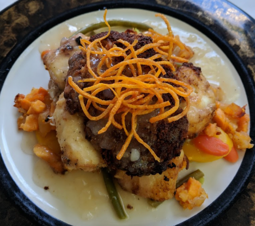 A plate of fried chicken topped with crispy onions, served with mixed vegetables and a creamy sauce.