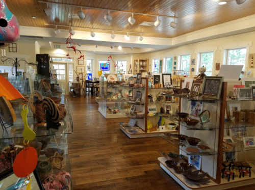 A cozy gift shop with wooden floors, displaying various crafts, artwork, and souvenirs on glass shelves.