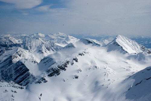 Snow-covered mountain peaks under a cloudy sky, showcasing a vast, rugged landscape.