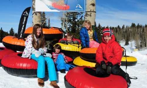 A group of five children sitting on colorful snow tubes in a winter landscape, smiling and enjoying the snowy day.