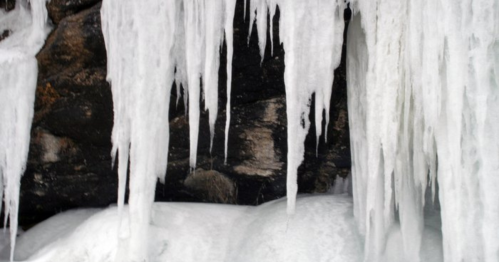 Icicles hanging from a rocky surface, with a layer of snow below, creating a wintery scene.