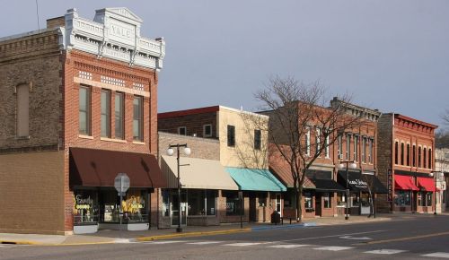 Historic downtown buildings with brick facades and awnings, lined along a quiet street under a cloudy sky.