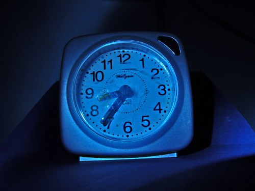 A square alarm clock with blue lighting, displaying the time in a dark setting.