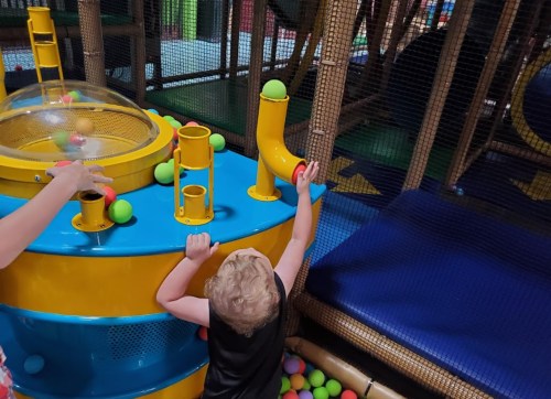 A child plays with colorful balls at a fun indoor playground activity station.
