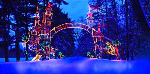 Colorful holiday lights form a whimsical castle archway in a snowy landscape, illuminated against a twilight sky.