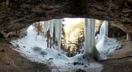 A cave opening with icicles hanging down, surrounded by snow-covered trees and a winter landscape.