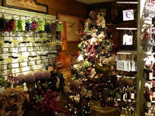 A cozy shop decorated for Christmas, featuring a tree, festive ornaments, and shelves of wine and grapes.