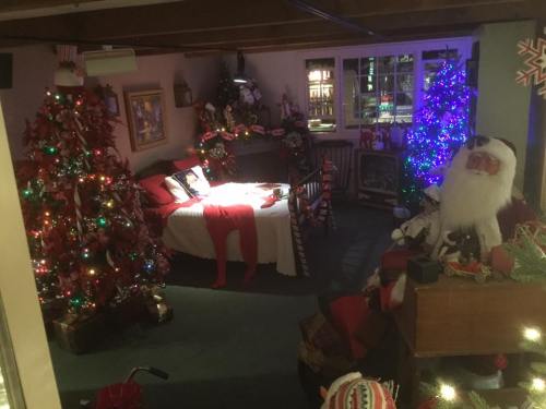 A cozy room decorated for Christmas, featuring colorful trees, festive lights, and a large Santa figure.